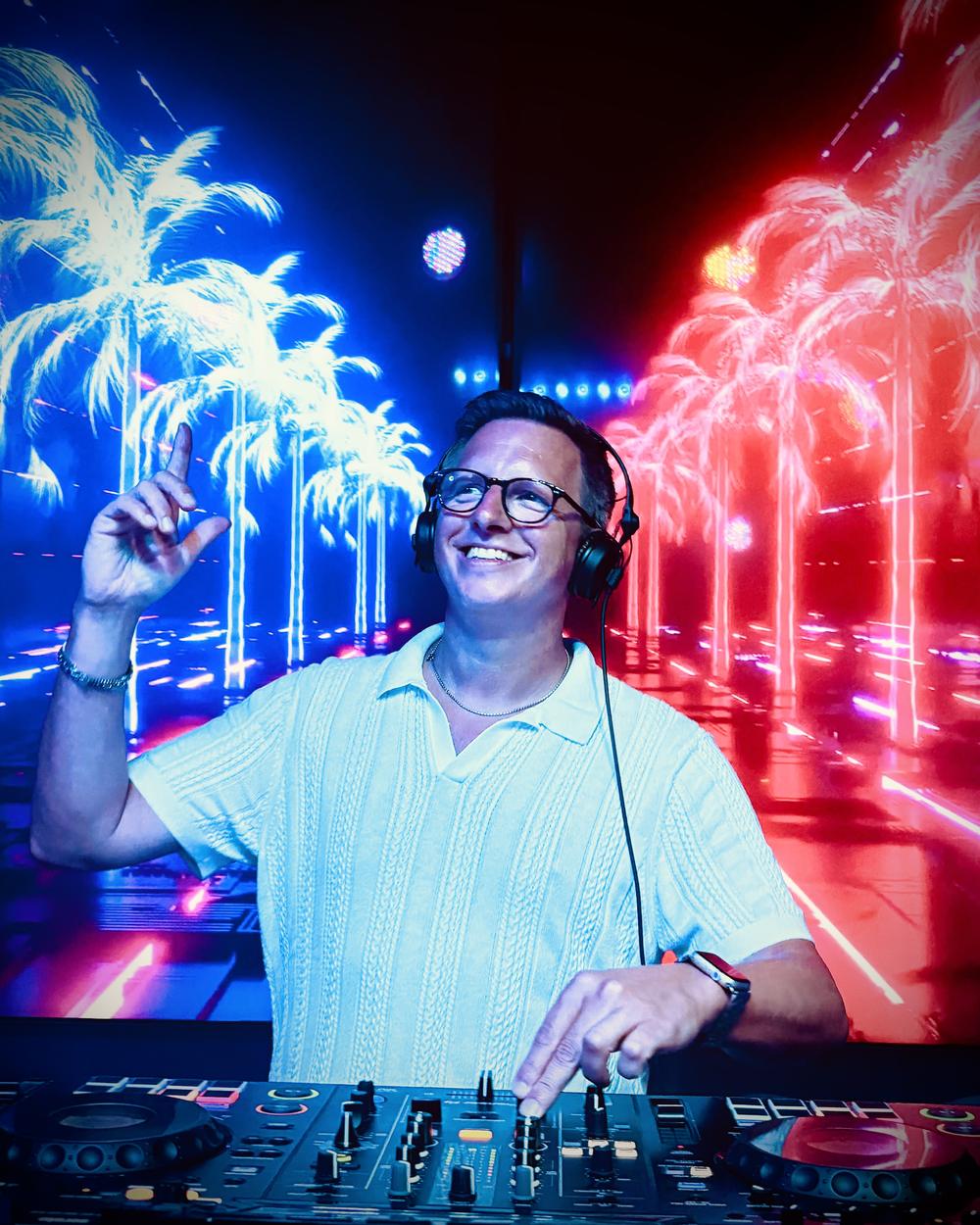 Jens Henrich alias DJ mcJay am DJ-Pult vor leuchtenden Palmen auf einer LED-Wand